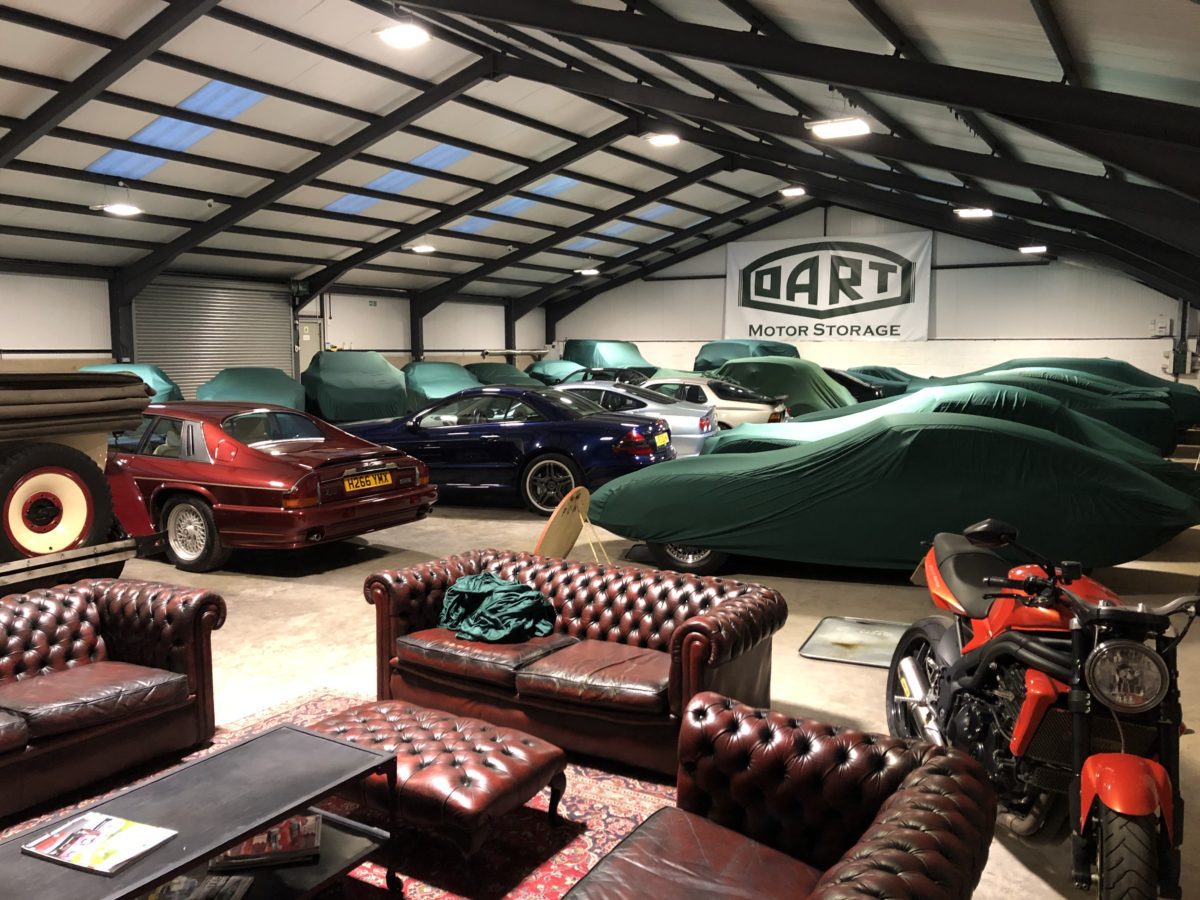 Various classic cars stored in an industrial warehouse unit with chesterfield sofas in the foreground.