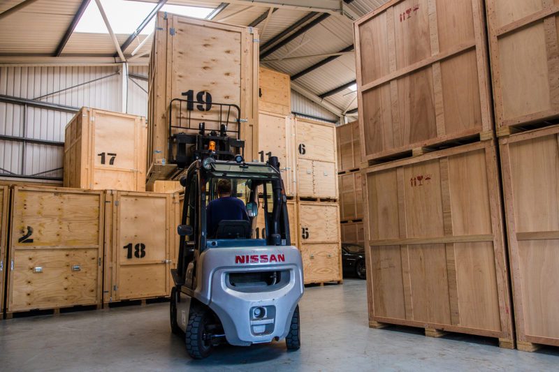 Wooden crate storage facility with a forklift truck lifting a crate into position.
