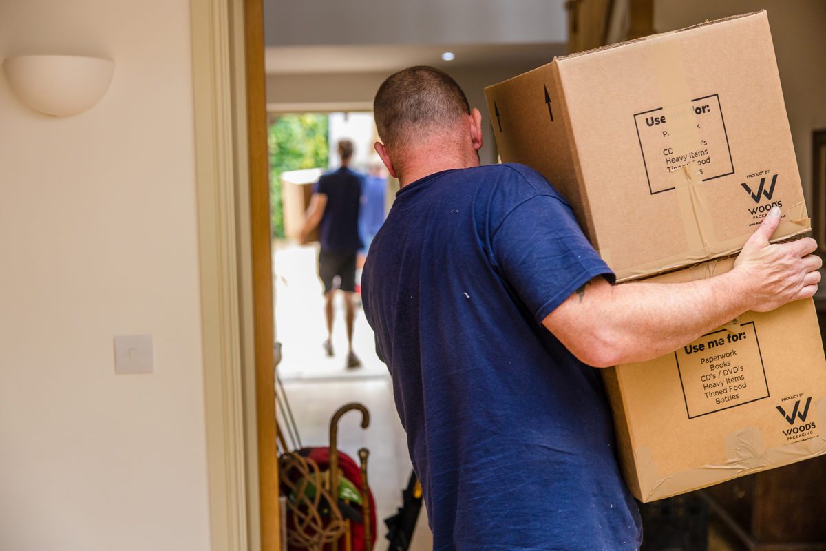 Removals person carrying boxes out of a house.