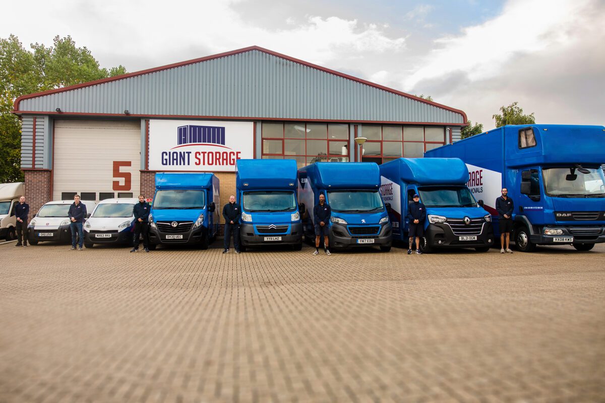 Giant Storage warehouse unit with branded removals vans parked outside and employees stood next to their respective vehicles.